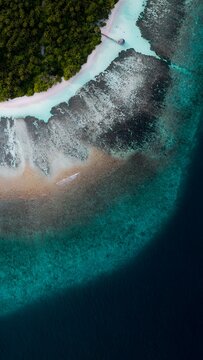 Aerial top view of tropical island coastline with turquoise ocean water and coral reef shelf