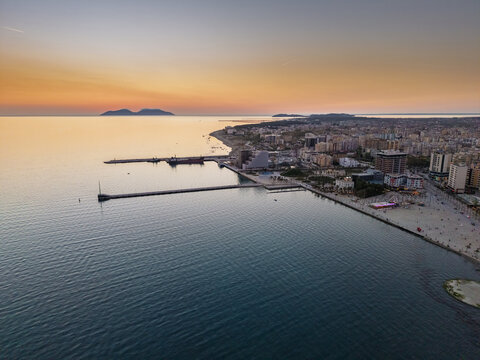 Aerial view of the Vlora waterfront and port area at sunset with calm sea, piers, and coastal buildings in Vlora, Vlore County, Albania.