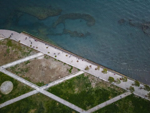 Aerial view of the coastal promenade featuring a paved walkway along the turquoise sea, green grassy areas, and people walking Vlora, Vlore County, Albania.
