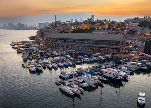 Aerial view of Jaffa Port with yachts and boats docked in the harbor at sunset, featuring historic stone buildings and the city skyline Tel Aviv-Jaffa, Tel Aviv District, Israel.