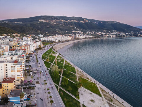 Aerial view of the Vlora coastline and Lungomare promenade, featuring modern apartment buildings, green park areas, and the calm sea at sunset in Vlora, Vlore County, Albania.