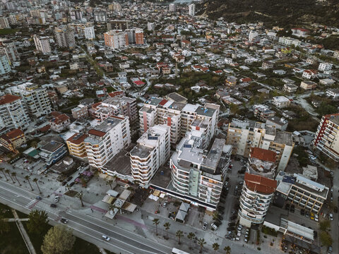 Aerial view of dense residential apartment buildings, a palm-lined waterfront road, and the surrounding landscape in Vlora, Vlore County, Albania.