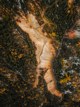 Aerial view of the Million Dollar Highway winding through a rugged mountain landscape with dense evergreen forests and golden autumn foliage in Ouray, Colorado, United States.