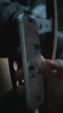 Close-up of tattooed hands scrolling or using a smartphone inside a car, with the steering wheel and dashboard. Mobile communication, digital technology, and online shopping. 4K.