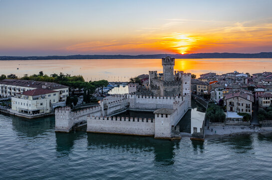 Aerial view of Castello Scaligero di Sirmione surrounded by the waters of Lake Garda at sunset with historic stone walls and rooftops in Sirmione, Lombardia, Italy.
