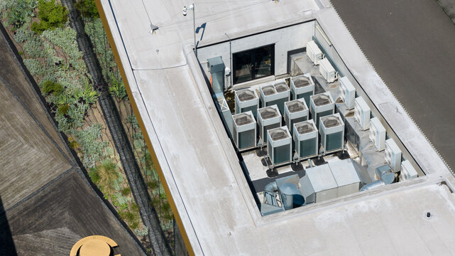 Aerial view of a flat roof with industrial HVAC units, adjacent to a green roof section with vegetation and a wooden deck in Houten, Utrecht, Netherlands.