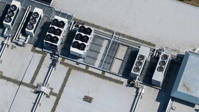Aerial view of industrial HVAC units on a flat roof, featuring cooling fans, metal piping, and ventilation systems on a grey industrial building surface in Nieuwegein, Utrecht, Netherlands.