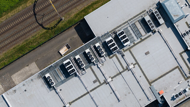 Aerial view of industrial building roof featuring multiple HVAC cooling units, adjacent railway tracks, and a small trailer in Nieuwegein, Utrecht, Netherlands.