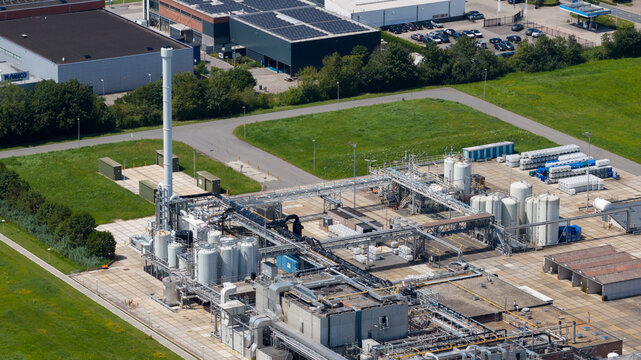 Aerial view of industrial facility featuring large storage tanks, complex piping systems, and storage containers in a paved yard in Zaltbommel, Gelderland, Netherlands.