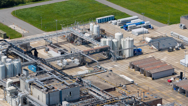 Aerial view of industrial facility featuring large storage tanks, complex piping systems, and storage containers in a paved yard in Zaltbommel, Gelderland, Netherlands.