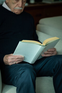 Close-up of an elderly man holding a book and reading at home