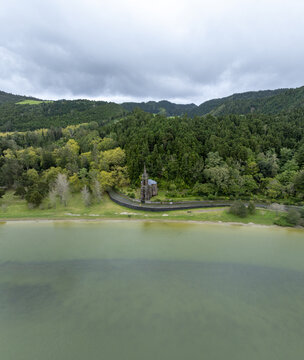 Aerial view of Ermida de Nossa Senhora das Vitorias situated on the shore of Furnas Lake, surrounded by lush green hills and forest in Furnas, Acores, Portugal.