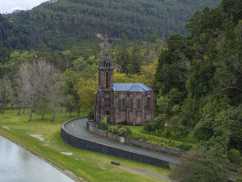 Aerial view of Ermida de Nossa Senhora das Vitorias, a neo-Gothic chapel situated by the lake and surrounded by lush forest and greenery in Furnas, Acores, Portugal.