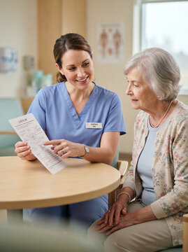 Nurse in blue scrubs explaining a care plan to an elderly woman at a table