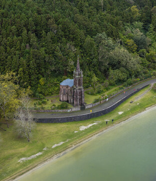Aerial view of the neo-Gothic Ermida de Nossa Senhora das Vitorias chapel nestled in lush forest beside the lake in Furnas, Acores, Portugal.