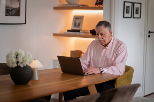 Confident senior man sitting at desk and using laptop in cozy scandinavian style home