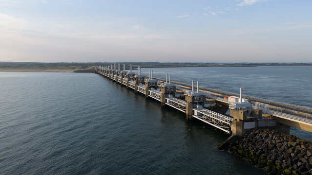 Aerial view of the Eastern Scheldt Storm Surge Barrier stretching across the water with concrete piers, steel gates, and rocky embankments in Vrouwenpolder, Zeeland, Netherlands.