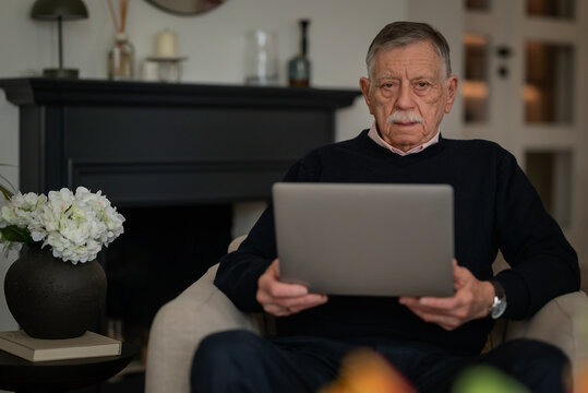 Concerned older man with laptop sitting in an armchair and checking finances online at home
