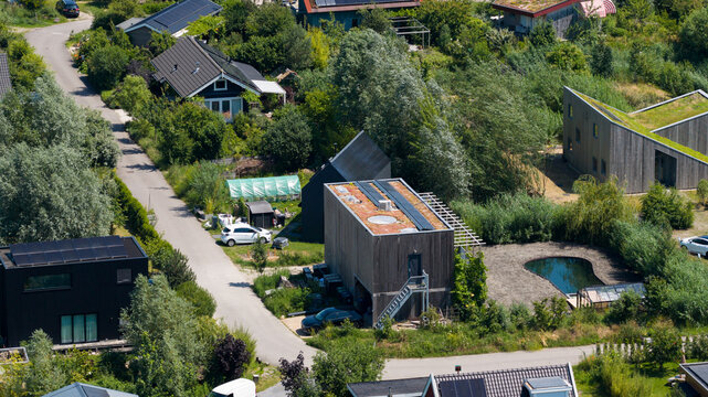Aerial view of Ecodorp Bolderburen featuring sustainable modern houses with green roofs and solar panels surrounded by lush greenery and a small pond in Almere, Flevoland, Netherlands.
