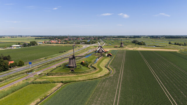 Aerial view of Bovenmolen G and surrounding historic windmills set amidst lush green agricultural fields and canals in Schermerhorn, Noord-Holland, Netherlands.