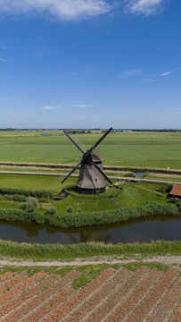 Aerial view of Bovenmolen G windmill surrounded by green fields, a canal, and agricultural land in Schermerhorn, Noord-Holland, Netherlands.