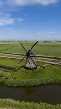 Aerial view of Bovenmolen G windmill surrounded by lush green fields and a canal in Schermerhorn, Noord-Holland, Netherlands.