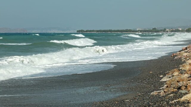 Beautiful view of storm waves crashing onto rocky beach against distant coastline. Crete. Greece.
