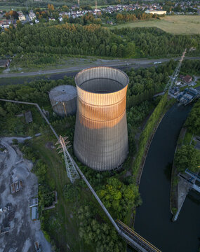 Aerial view of the abandoned Power Plant IM cooling tower surrounded by lush greenery and a canal in Charleroi, Wallonia, Belgium.