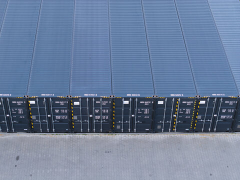 Aerial view of rows of blue shipping containers arranged in a neat line on a paved industrial yard in Poland.