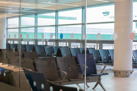 Empty seats in airport waiting hall viewed through glass wall during flight delays.