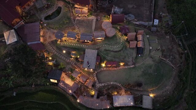 Aerial view of a resort area in Trawas with illuminated pathways, small thatched-roof structures, and lush greenery at dusk in Trawas, East Java, Indonesia.