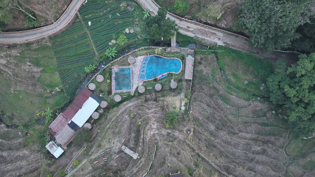 Aerial view of a swimming pool complex nestled among terraced rice fields and lush greenery in Trawas, East Java, Indonesia.