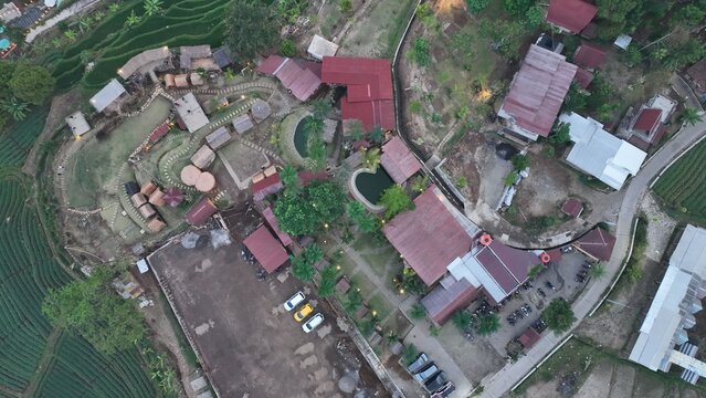 Aerial view of a resort in Trawas featuring small cabins, a parking area, and lush green rice terraces in the mountainous landscape of Trawas, East Java, Indonesia.