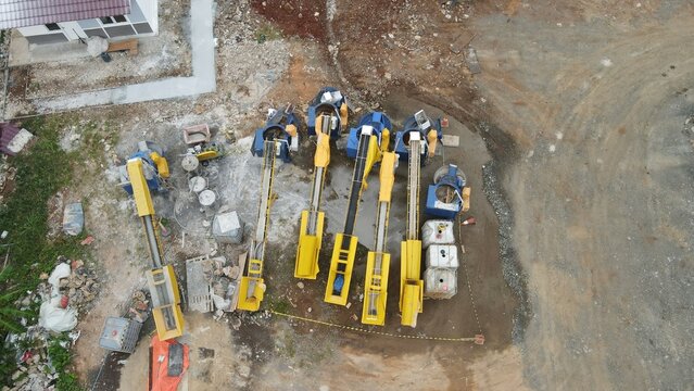 Aerial view of construction machinery including yellow conveyor belts and mixers positioned on a dirt site at Bambu Apus in Kecamatan Cipayung, Daerah Khusus Ibukota, Indonesia.