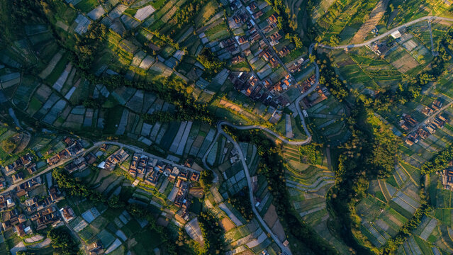 Aerial view of the village of Selo surrounded by terraced agricultural fields and winding roads in the lush landscape of Selo, Central Java, Indonesia.