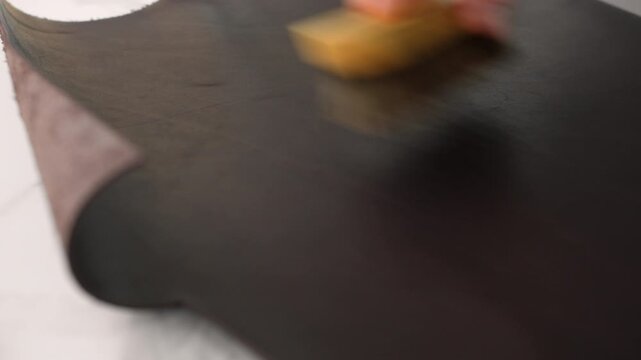 Artisan shoemaker brushing genuine brown leather with a tool in a traditional workshop for shoe or bag making