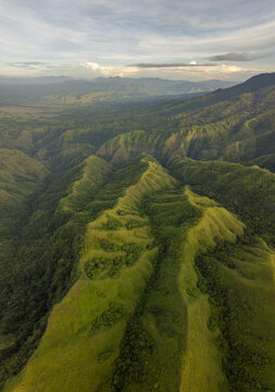 Aerial view of Avatar Hill Watu Nari Wowo featuring lush green ridges, deep valleys, and rolling hills under a soft sky in Bajawa, East Nusa Tenggara, Indonesia.