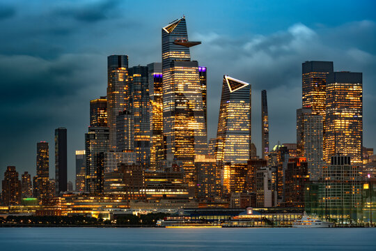 Night view of the Midtown Manhattan skyline in New York City showcasing the modern illuminated skyscrapers of the Hudson Yards real estate developments across the water.