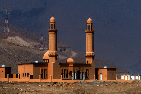 View of a mosque with two minarets and orange walls set against a rugged mountain landscape in Muscat, Muscat Governorate, Oman.