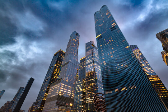 Low angle view from below looking up at massive illuminated skyscrapers of the Hudson Yards real estate development in midtown Manhattan under dramatic dusk sky in New York City.