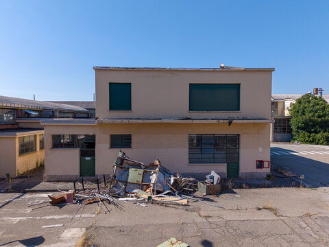 Aerial view of an old industrial building with boarded windows and scattered debris on the asphalt ground under a clear blue sky in Casale Monferrato, Piedmont, Italy.
