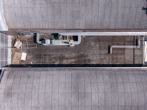 Aerial view of a flat industrial roof section between two corrugated metal roofs with ventilation equipment and pipes in Casale Monferrato, Piedmont, Italy.