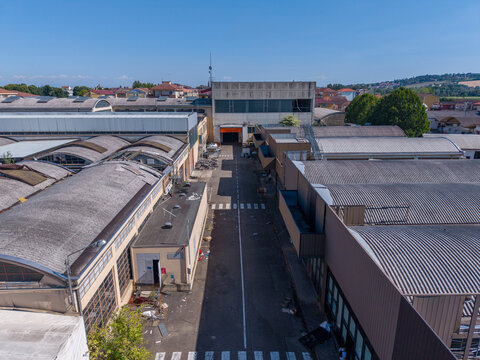 Aerial view of the industrial complex featuring large warehouses with corrugated metal roofs and a central access road in Casale Monferrato, Piedmont, Italy.