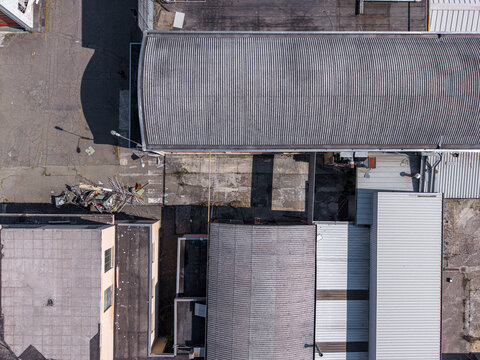 Aerial view of industrial buildings with corrugated metal roofs and concrete courtyards in an urban setting in Casale Monferrato, Piedmont, Italy.