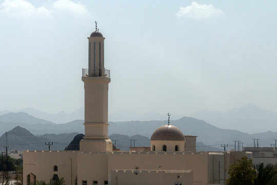 View of a mosque featuring a tall minaret and a central dome set against a backdrop of rugged mountains in Muscat, Muscat Governorate, Oman.