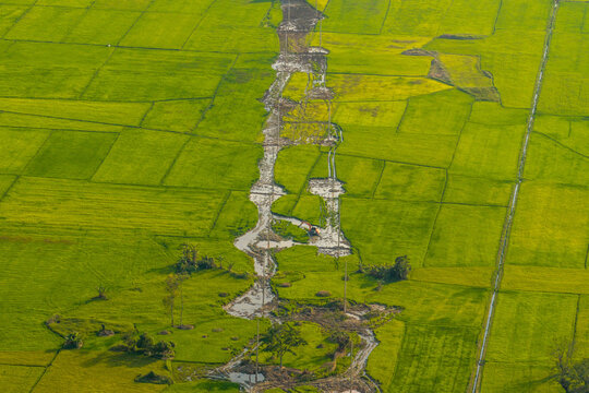 Aerial view of the lush green rice paddies surrounding Lak Lake, featuring intricate irrigation channels and rural agricultural land in Lien Son Lak, Dak Lak, Vietnam.