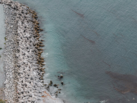Aerial view of the concrete breakwater protecting the coastline with calm dark waters and kelp beds in Unalaska, Alaska, United States.