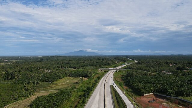 Aerial view of Jalan Tol Terbanggi Besar - Pematang Panggang - Kayu Agung highway through green landscape and palm oil plantations in Kecamatan Lempuing Jaya, Sumatera Selatan, Indonesia.