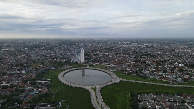 Aerial view of the circular lake and tall building in Summarecon Bekasi surrounded by dense urban residential areas in Bekasi Barat, West Java, Indonesia.