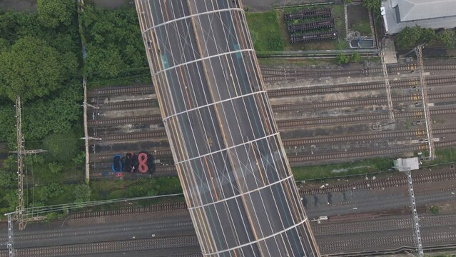 Aerial view of a railway bridge crossing over multiple train tracks in an urban area in Bekasi Barat, West Java, Indonesia.